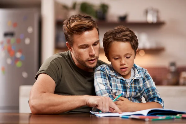 Батьки - перші і найважливіші вчителі. Постріл чоловіка, що сидить зі своїм сином, поки він робить домашнє завдання . — стокове фото