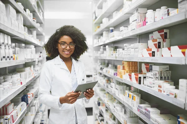 У нас є всі ліки, які знадобляться будь-кому. Портрет веселого молодого жіночого фармацевта, що стоїть з цифровим планшетом, дивлячись на камеру в аптеці . — стокове фото