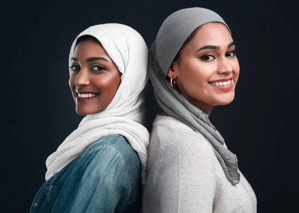 We zullen elkaar altijd steunen. Gehakt schot van twee aantrekkelijke jonge vrouwen dragen hijabs en staan rug aan rug tegen een zwarte studio achtergrond. — Stockfoto