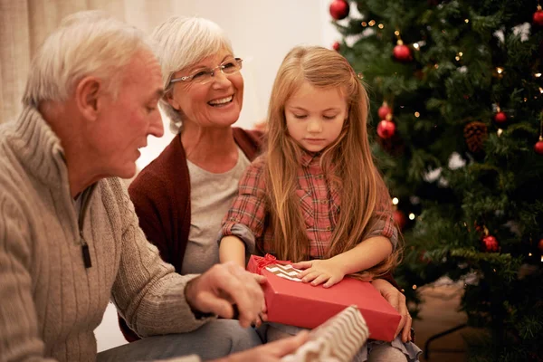 I wonder whats in this one. Shot of a little girl spending Christmas with her grandparents. — ストック写真