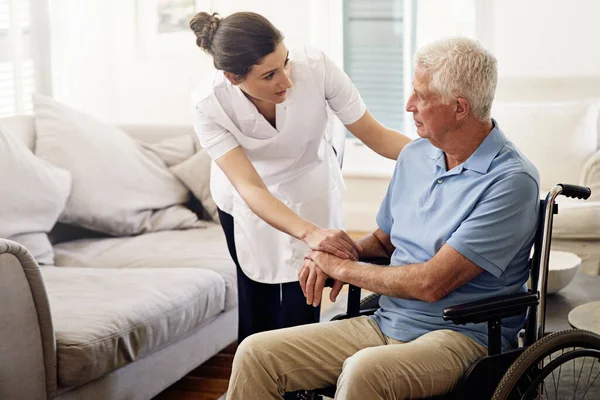 Ajudando-o durante todo o dia. Tiro de um cuidador ajudando um homem idoso em uma cadeira de rodas em casa. — Fotografia de Stock
