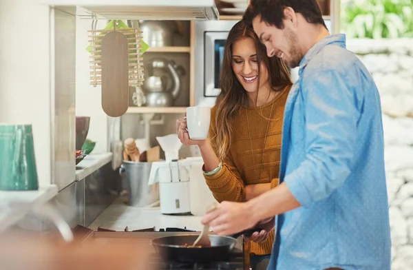 O que estás a fazer. Tiro de uma jovem mulher atraente assistindo seu namorado cozinhar em sua cozinha. — Fotografia de Stock