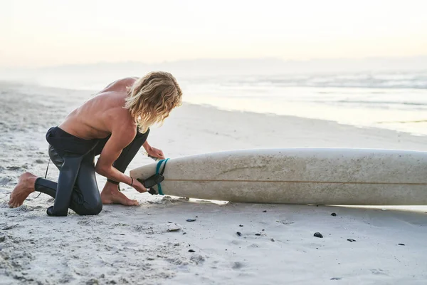 Preparándose para un gran día en el furioso océano. Tiro de longitud completa de un joven surfista guapo preparando su tabla de surf antes de ir a surfear en la playa. —  Fotos de Stock