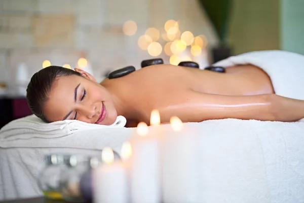 Take a vacation on our massage table. Shot of a young woman enjoying a hot stone massage at a spa. — Stock Photo, Image