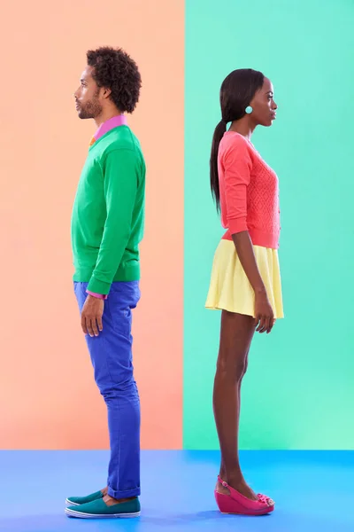Not quite complete opposites. Studio shot of a young couple standing against a colourful background. — ストック写真