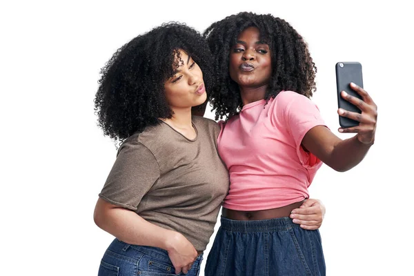 Bästa vänner gör de bästa profilbilderna. Studio skott av två unga kvinnor som använder en smartphone för att ta selfies mot en vit bakgrund. — Stockfoto