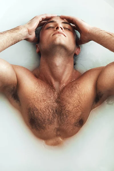 Let the milkiness submerge you. High angle shot of a handsome young man lying in a bathtub full of milky water at home. — Stock Photo, Image