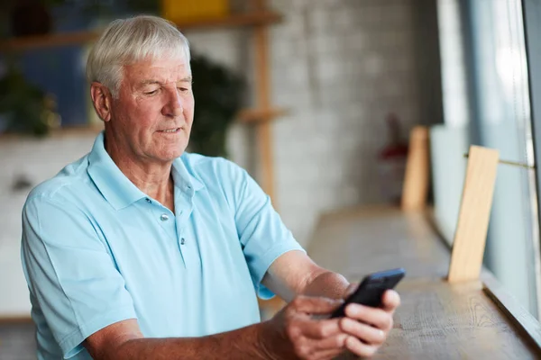 Estoy esperando en la cafetería. Recorte de un hombre mayor usando su teléfono celular mientras está sentado en una cafetería. —  Fotos de Stock