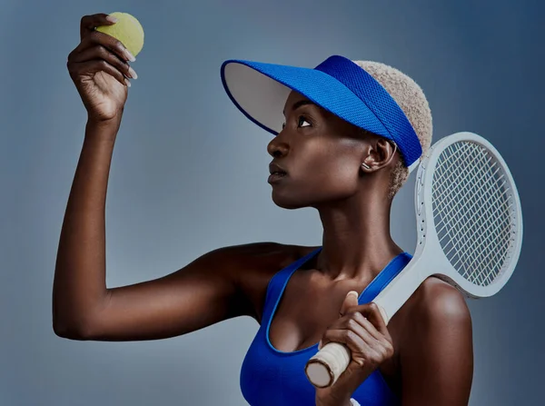 Tennis is the answer. Studio shot of a sporty young woman posing with tennis equipment against a grey background. — Photo