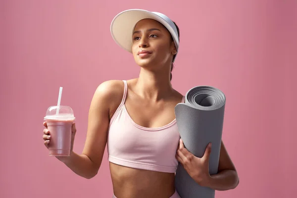 Its about living a balanced life. Cropped shot of an attractive and sporty young woman posing with an exercise mat and a smoothie in studio against a pink background. — 스톡 사진