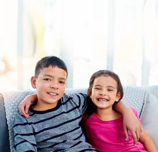 我们比你想象的要接近。两个年轻可爱的兄弟姐妹抱着胳膊在家里沙发上放松时的画像. — 图库照片