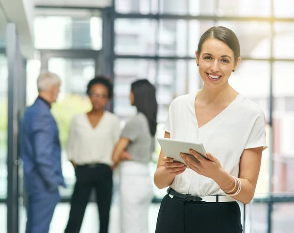 Her passion for business is so inspiring. Portrait of a young businesswoman holding a digital tablet with her colleagues in the background. — Photo