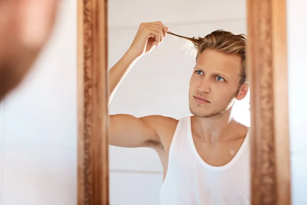 Maybe its time I chopped it all off. Shot of a young man looking at his hair in the mirror at home. — Foto de Stock
