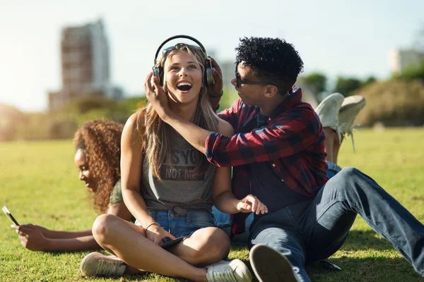 Ouve-me. Tiro de dois jovens amigos alegres ouvindo música em fones de ouvido fora em um parque durante o dia. — Fotografia de Stock