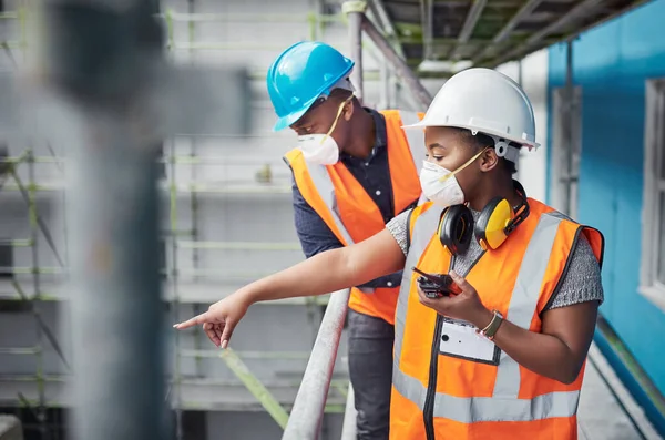 Évoluer de nouveaux sommets dans le secteur de la construction. Prise de vue d'une jeune femme utilisant un talkie-walkie alors qu'elle travaillait avec son collègue sur un chantier de construction. — Photo