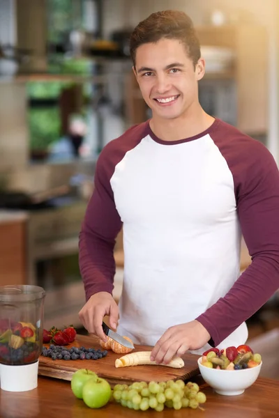 O seu saboroso e nutritivo. Retrato de um jovem feliz preparando um saudável café da manhã de frutas em sua cozinha em casa. — Fotografia de Stock