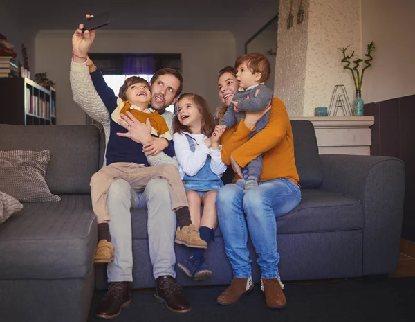 Selfie familiar. Largura completa de una familia joven y cariñosa de cinco tomando selfies en el sofá en casa. —  Fotos de Stock