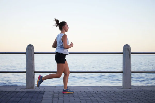 Dont talk about it, just do it. Shot of a sporty young woman out for a run on the promenade. — Stock Photo, Image