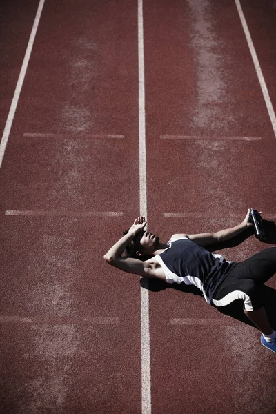 Het leven in de fast lane is vermoeiend. Een jonge loper liggend op de tartan baan. — Stockfoto