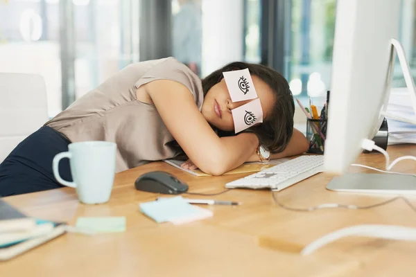 Time for a catnap. Shot of a tired businesswoman napping at her desk with adhesive notes on her eyes. — Stock Photo, Image