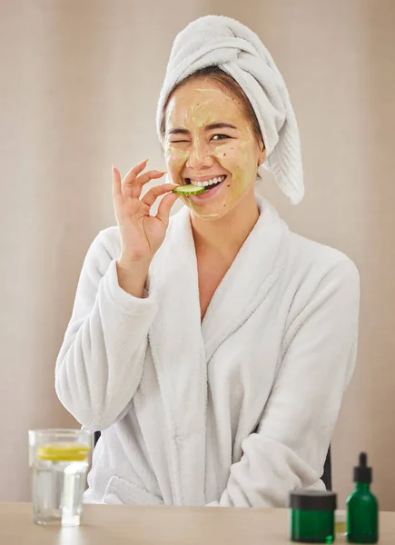 Um fim-de-semana de auto-cuidado. Tiro de uma jovem mulher comendo um pepino enquanto faz um tratamento de beleza facial em casa. — Fotografia de Stock