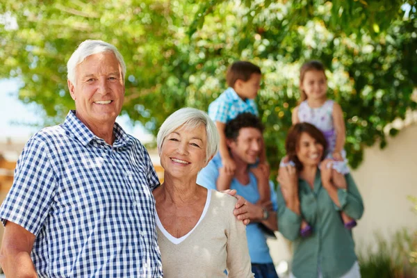 El amor de una familia es la mayor bendición de la vida. Foto de una feliz pareja de ancianos con su familia de pie en el fondo. — Foto de Stock