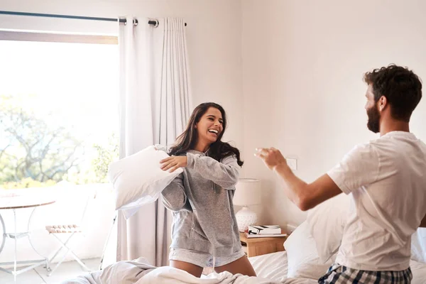 Comece todas as manhãs com tolice. Tiro de um jovem casal feliz ter uma luta travesseiro na cama. — Fotografia de Stock