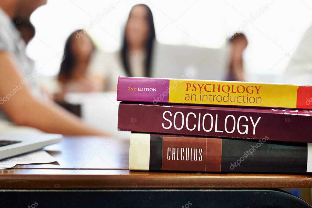 Social Studies. Cropped shot of university text books on a desk with students blurred in the background.