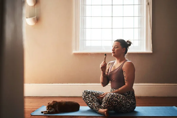 O cheiro deixará alguns efeitos mágicos em você. Tiro de uma jovem mulher queimando um pau palo santo enquanto sentado em um tapete de ioga ao lado de seu cão em casa. — Fotografia de Stock