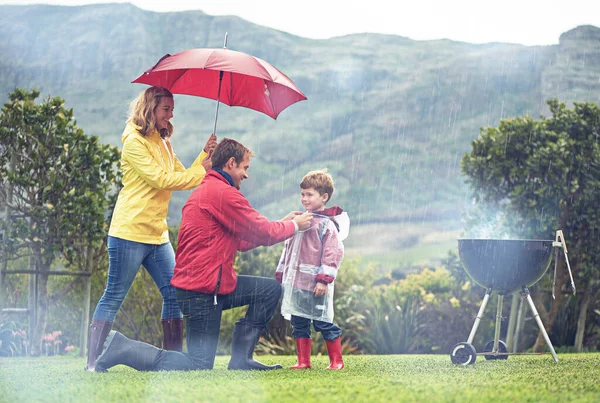 Deszcz nie powstrzyma ich od zabawy. Zdjęcie rodziny urządzającej grilla na zewnątrz w deszczową pogodę. — Zdjęcie stockowe