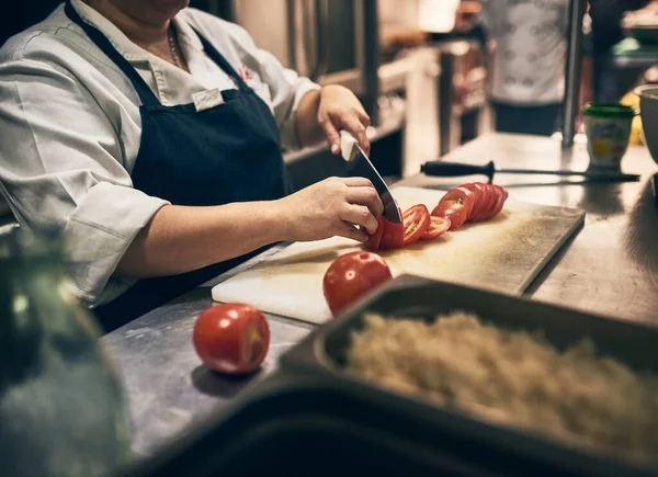 Corta e corta. Tiro de um chef irreconhecível cortando tomates com uma faca em uma placa em uma cozinha. — Fotografia de Stock