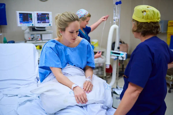 Voorbereiding van de laatste fasen voor de operatie. Shot van een jonge zwangere vrouw zitten op haar ziekenhuisbed en op zoek bedachtzaam met verpleegkundigen op de achtergrond. — Stockfoto