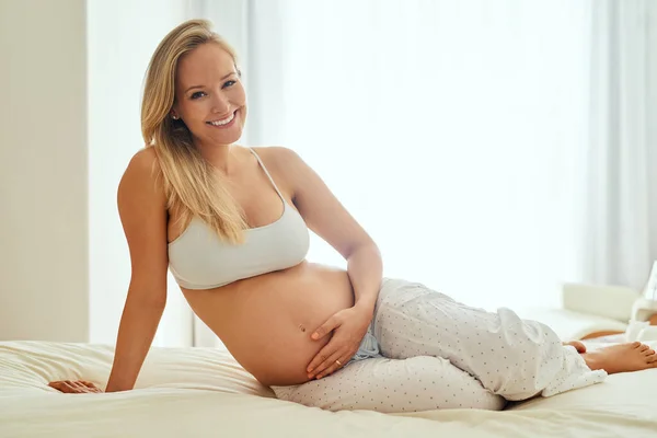 Gelukkige moeders maken gelukkige baby 's. Schot van een zwangere vrouw die haar buik aanraakt terwijl ze op haar bed zit. — Stockfoto
