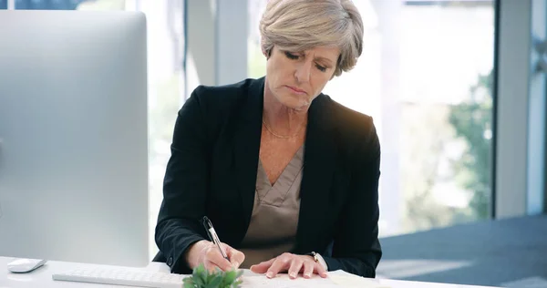 Це зайнятий день в офісі. Постріл зрілої бізнес-леді писати нотатки під час роботи на комп'ютері в офісі . — стокове фото