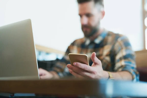 Neem uw draadloze apparaten overal mee naartoe. Foto van een jonge man met behulp van zijn mobiele telefoon en laptop tijdens het zitten in een cafe. — Stockfoto