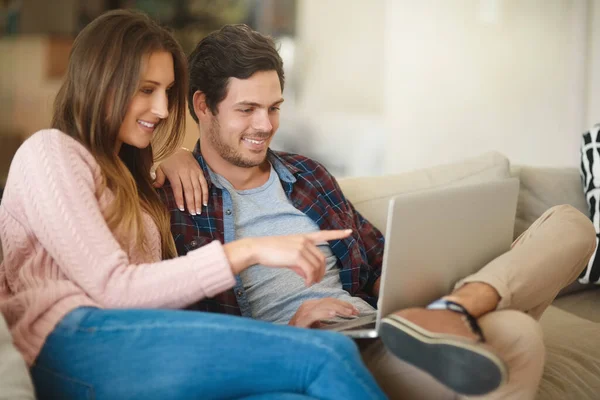 House hunting from the comfort of their couch. Shot of a happy young couple using a laptop together while relaxing on the sofa at home. —  Fotos de Stock