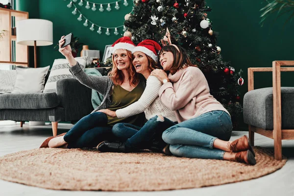 Dieses hier geht auf das Album. Aufnahme von drei attraktiven Frauen mittleren Alters, die in der Weihnachtszeit zu Hause mit einem Handy Selbstporträts machen. — Stockfoto