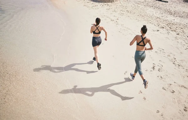 Dejando su huella en la pista. Alto ángulo de tiro de dos mujeres jóvenes atléticas irreconocibles para una carrera en la playa. —  Fotos de Stock