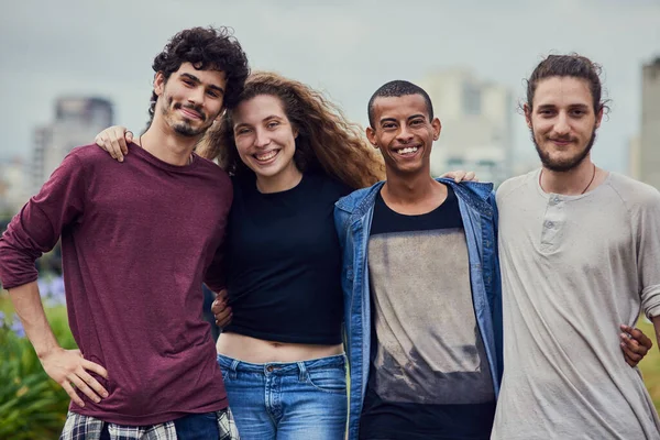 Universitetet er flott når man har slike venner. Portrett av en gruppe unge studenter som står rundt hverandre utenfor i en park om dagen. – stockfoto