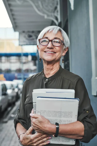 Deze stad herinnert me altijd aan mijn jeugd. Portret van een vrolijke volwassen zakenvrouw met boeken en papierwerk in de stad. — Stockfoto