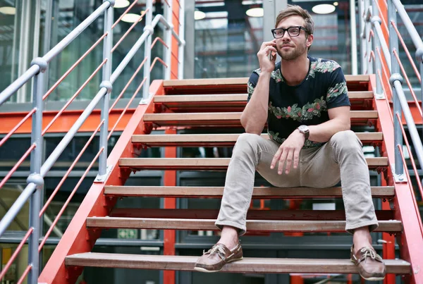 Staying in touch with his clients. Shot of a handsome young man using his mobile phone while sitting on the steps of an office. — Stock Photo, Image