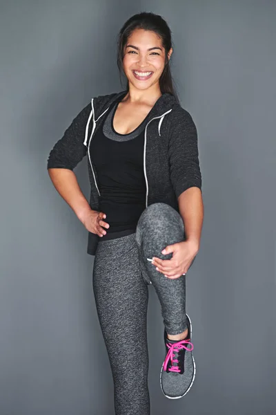 Shes a fitness enthusiast. Shot of a fit young woman stretching her legs against a gray background. — Stock Photo, Image