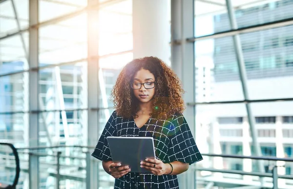 Handling her business the smart way. Cropped shot of an attractive young businesswoman using a digital tablet while standing in a modern office. — Stock Photo, Image