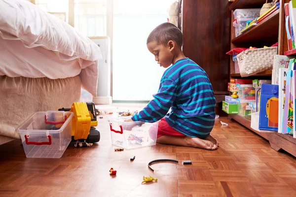 Playing and packing. Shot of a young boy sitting on the floor with toys in a bedroom. — Stock Photo, Image