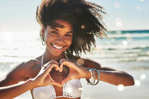 O meu coração pertence ao verão. Retrato de uma bela jovem mulher fazendo um gesto em forma de coração com as mãos na praia. — Fotografia de Stock