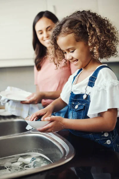 Chores gehören zum Erwachsenwerden dazu. Aufnahme eines entzückenden jungen Mädchens, das zu Hause seiner Mutter beim Geschirr in der Küche hilft. — Stockfoto