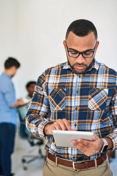 Het voldoen aan zijn leidinggevende taken met moderne technologie. Foto van een jonge ondernemer met behulp van een digitale tablet op het werk met zijn team op de achtergrond. — Stockfoto