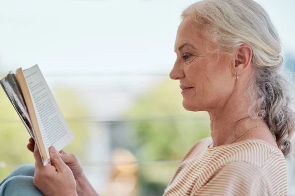 Estresse menos, leia mais. Tiro de uma mulher madura lendo um livro em sua varanda em casa. — Fotografia de Stock