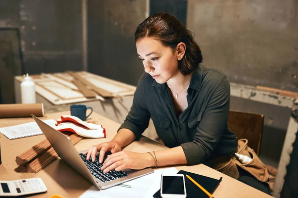 Di nuovo sui libri contabili. Ritagliato colpo di un attraente giovane falegname femminile che lavora sul suo computer portatile in officina. — Foto Stock