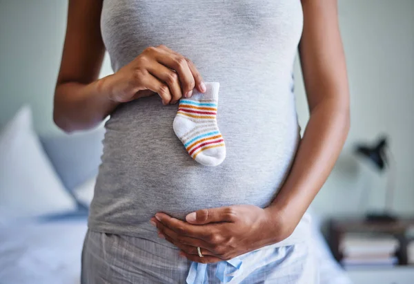 Malé nožičky potřebují malé ponožky. Vystřižený záběr těhotné ženy držící kojeneckou ponožku před břichem. — Stock fotografie